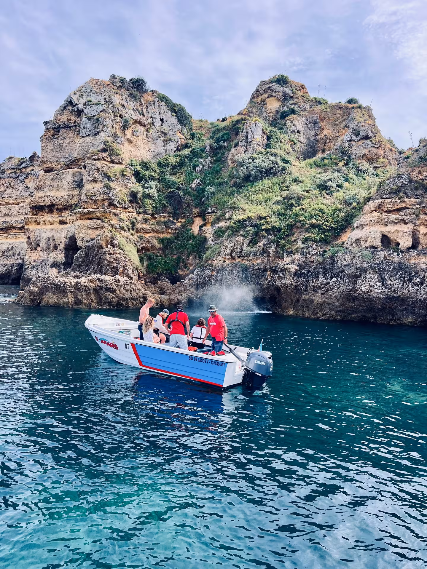 Small tour boat with guests exploring dramatic golden cliffs and sea caves at Ponta da Piedade Lagos Algarve Portugal