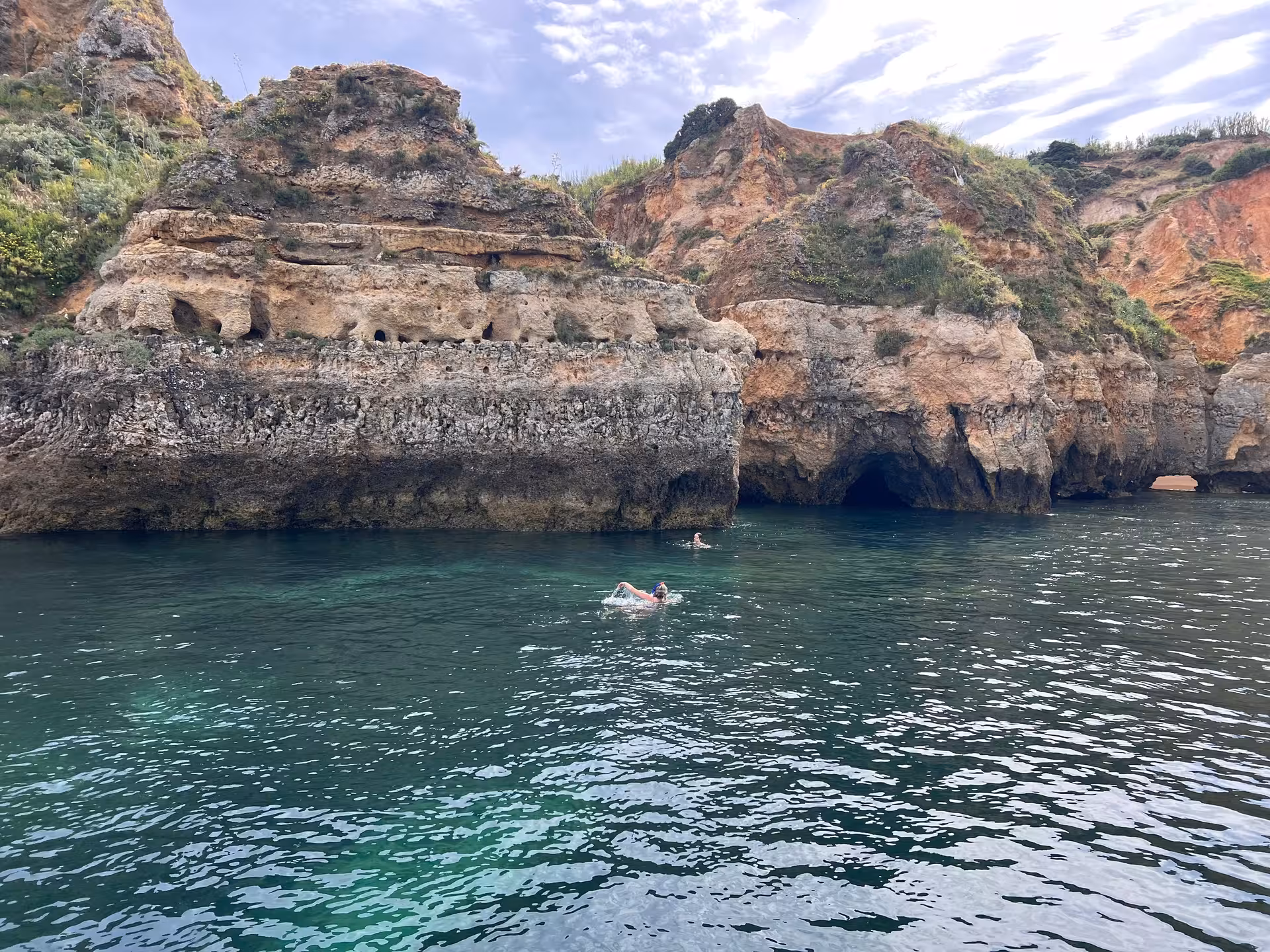 Swimmers exploring emerald green waters beside stunning Ponta da Piedade sea caves and cliffs in Lagos Portugal