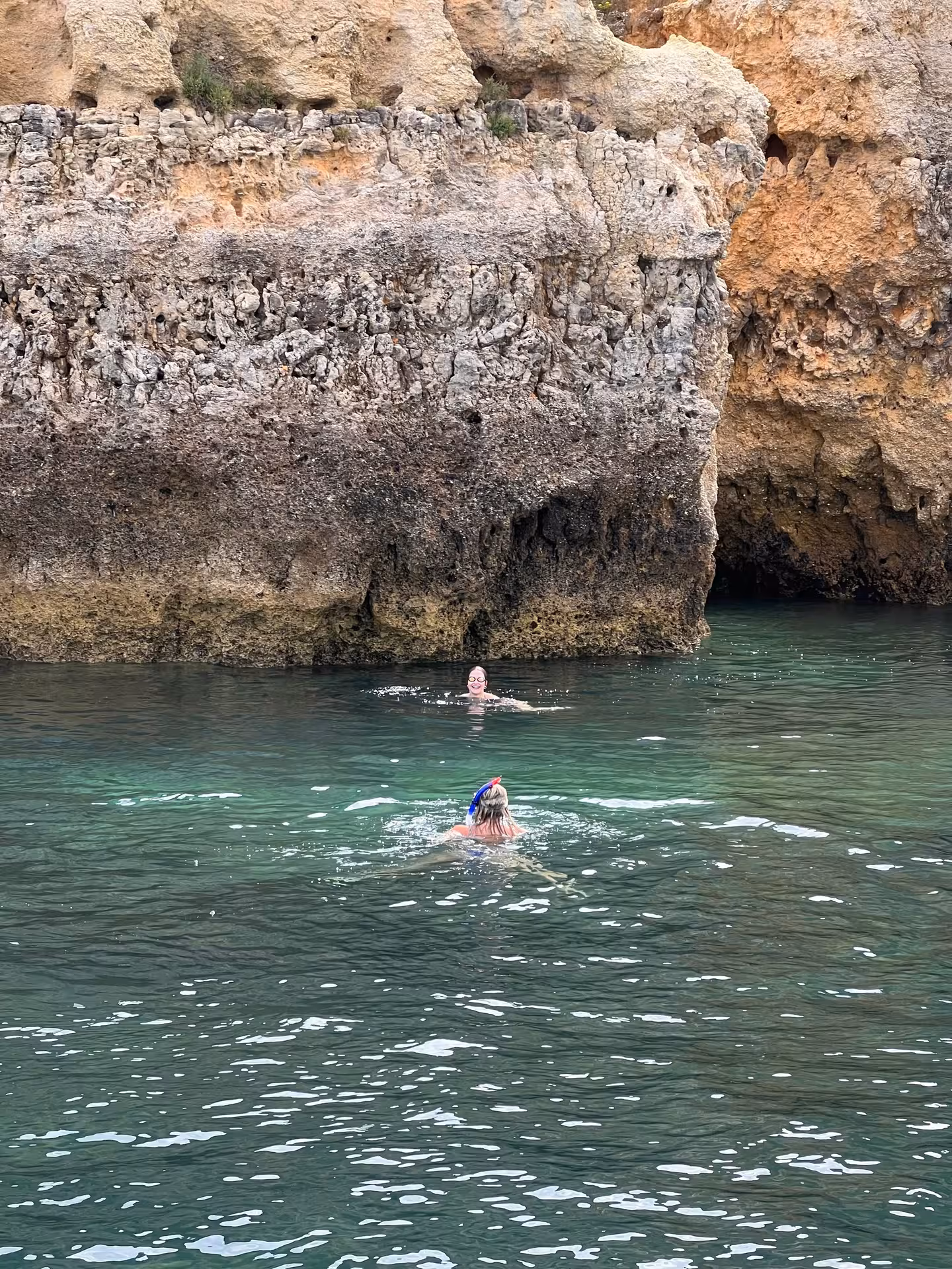 Two swimmers snorkeling in turquoise waters beside golden limestone sea caves on a Ponta da Piedade Lagos boat tour