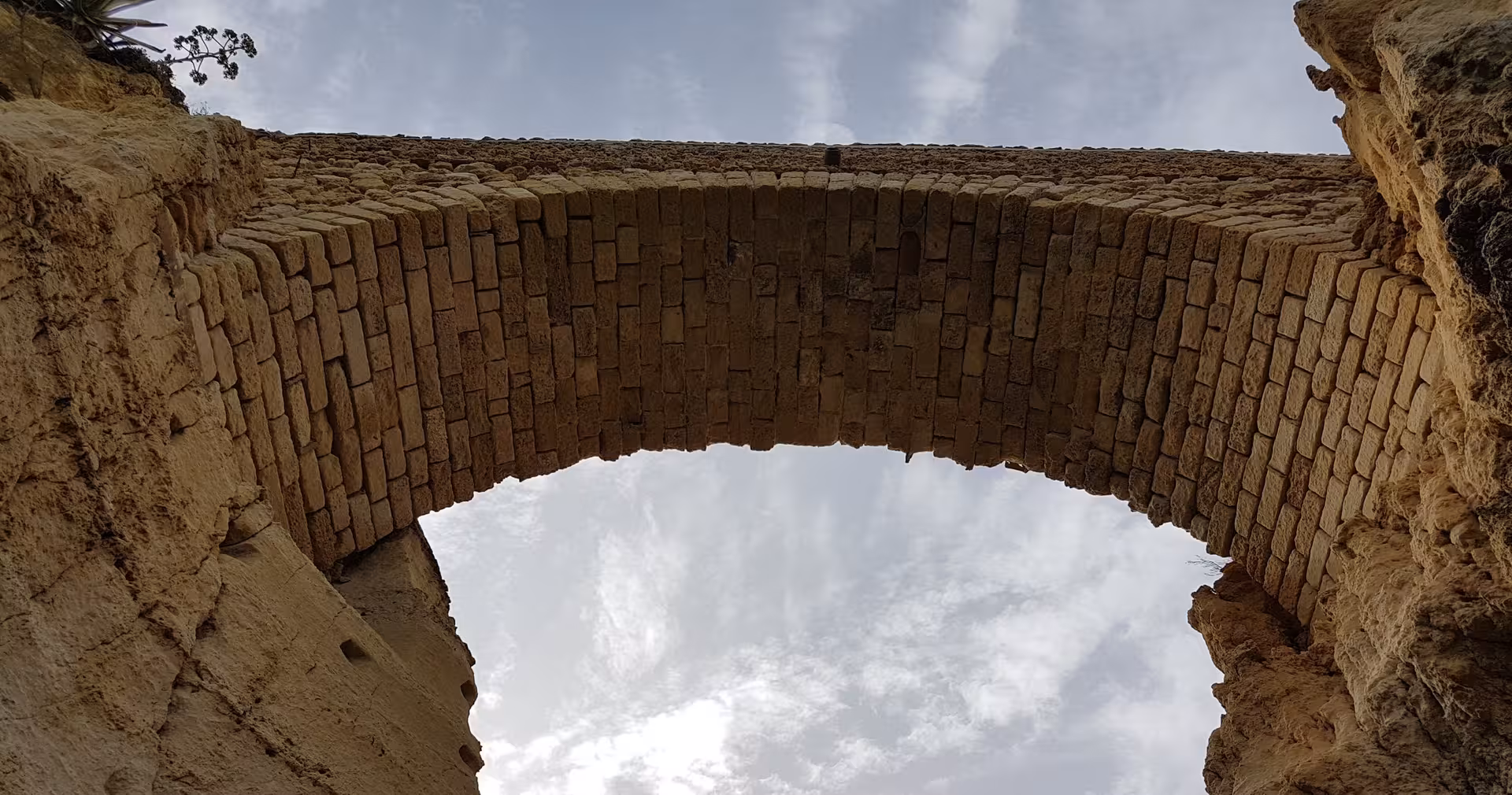 Upward view of ancient stone archway carved into Ponta da Piedade cliffs in Lagos, Algarve against a bright coastal sky
