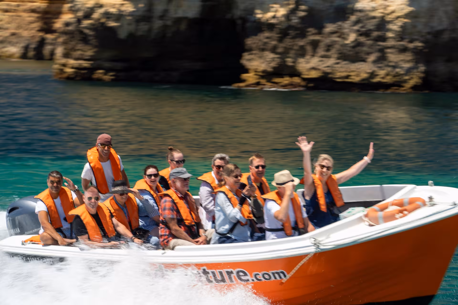 Excited tourists in orange life jackets enjoying a Ponta da Piedade cave boat tour on turquoise waters in Lagos Portugal