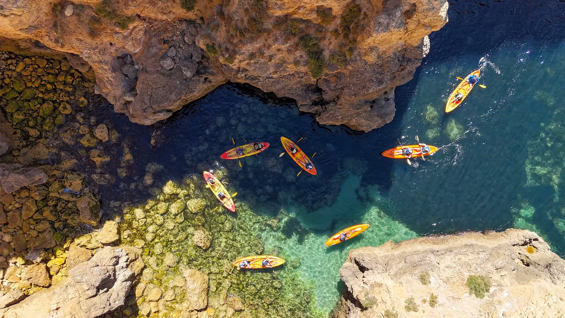 Drone view of a guided kayak tour group paddling among dramatic golden limestone cliffs and sea caves at Ponta da Piedade Algarve Portugal