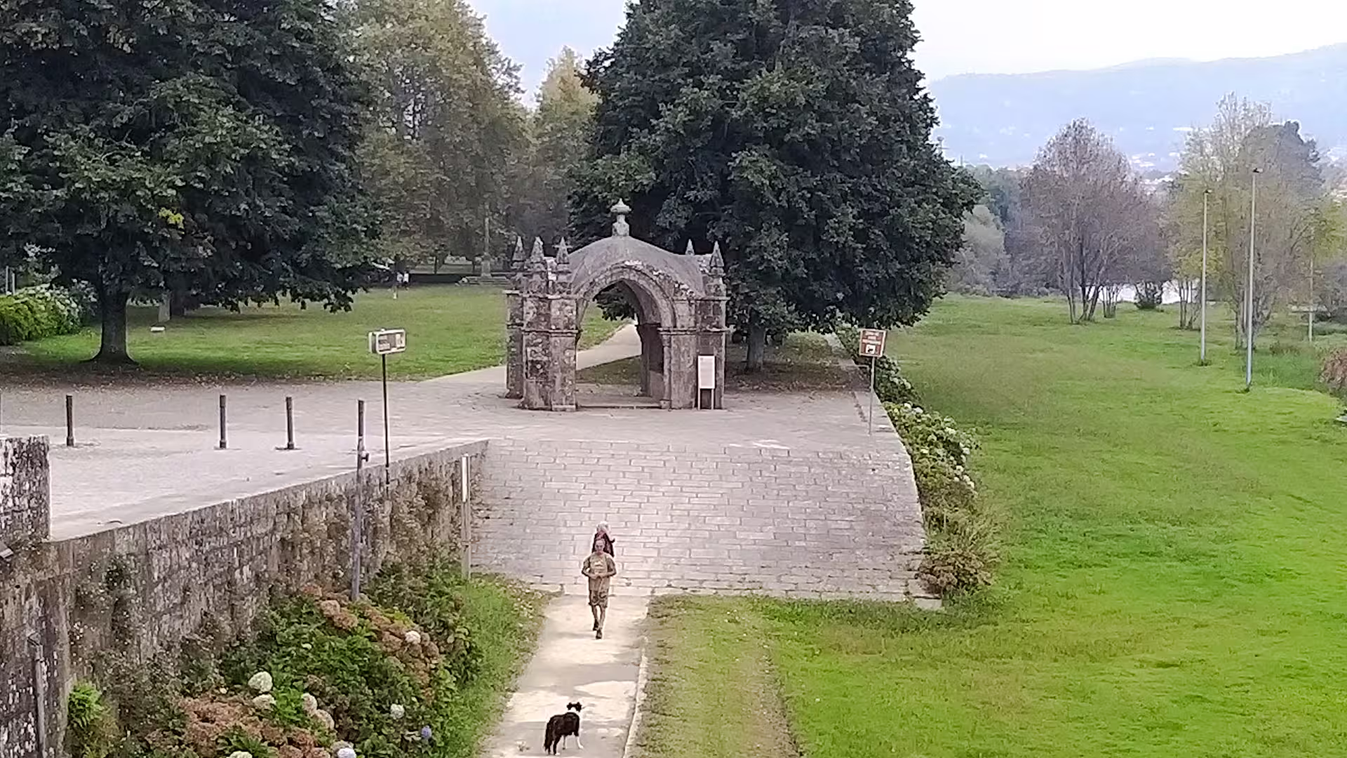 A serene pathway in Ponte de Lima's lush landscape, featuring an ancient stone arch and a leisurely stroll with a dog, perfect for exploring the Vinho Verde region.