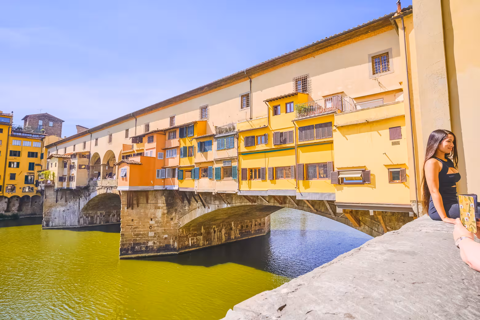 View of the iconic Ponte Vecchio in Florence with colorful buildings and tourists, highlighting a key walking tour site.
