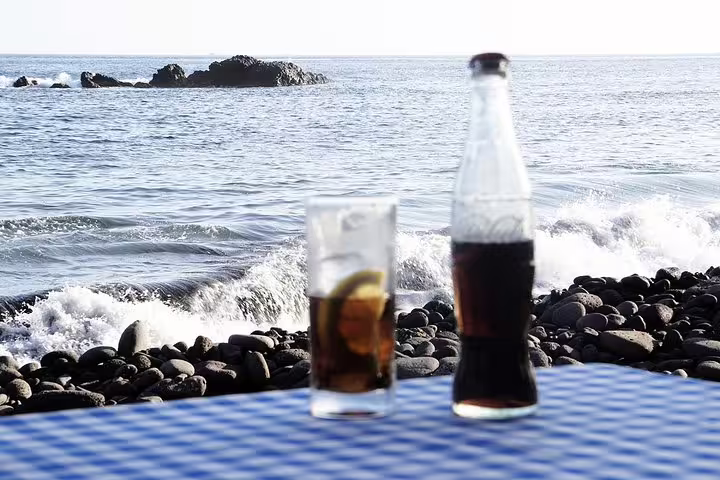 Refreshing local Pontxi drink on a beachfront table in Praia, Cape Verde, with ocean waves and rocky shoreline in the background.