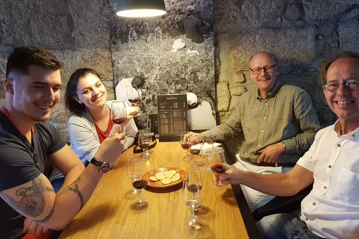 Smiling group of friends toasting with glasses of port and Douro wines, seated around a wooden table with snacks.