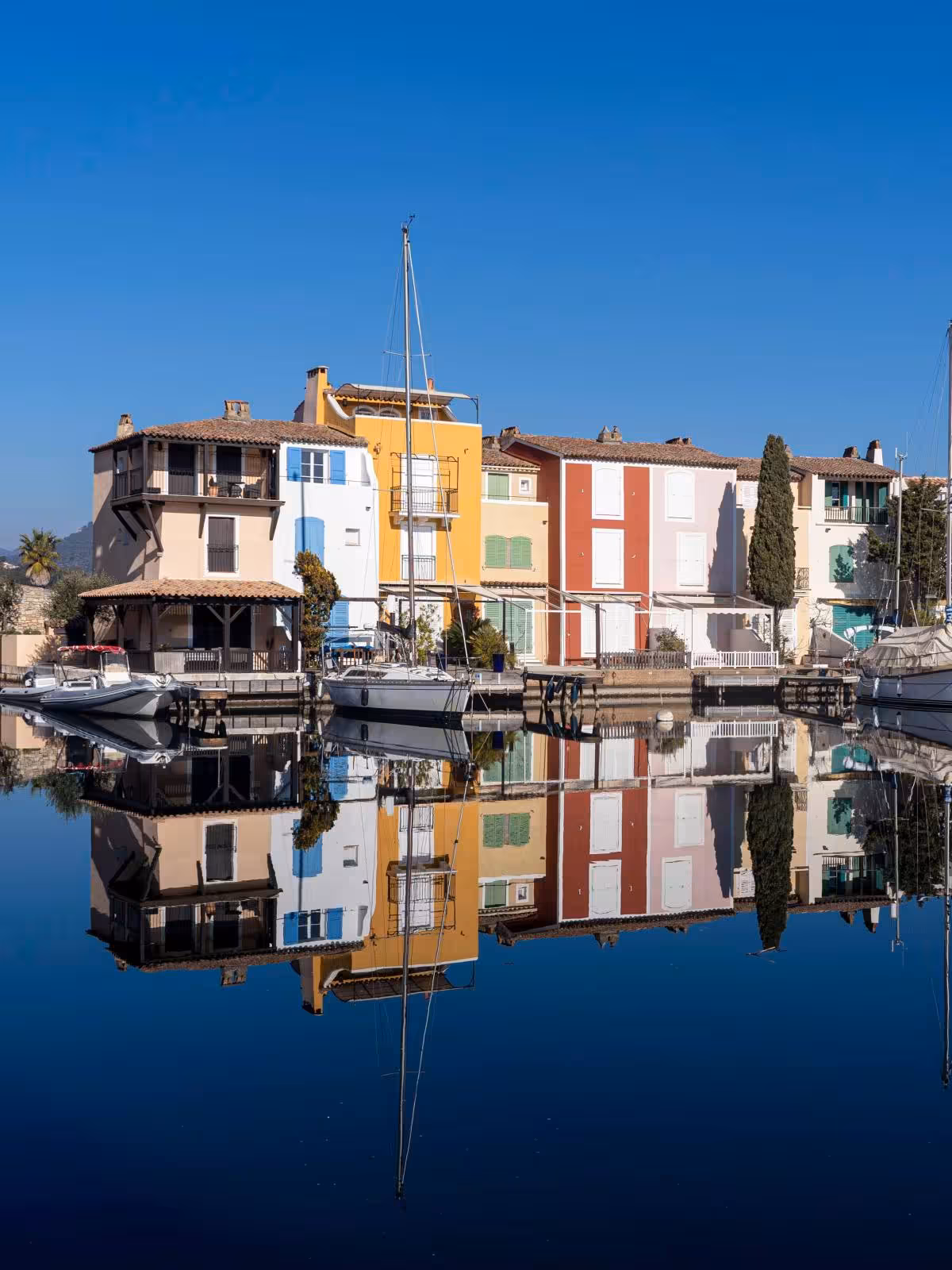 Colorful waterfront houses and sailboats reflected in calm canal waters of Port Grimaud, French Riviera
