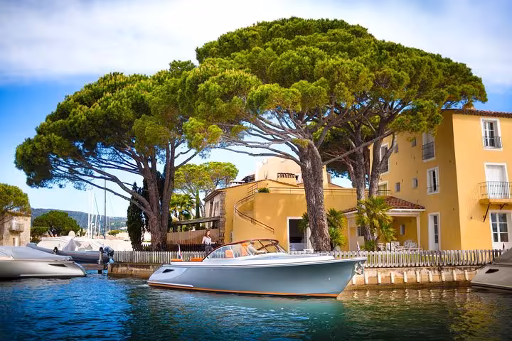 Luxury white speedboat docked at Port Grimaud marina with yellow Provençal buildings and umbrella pine trees