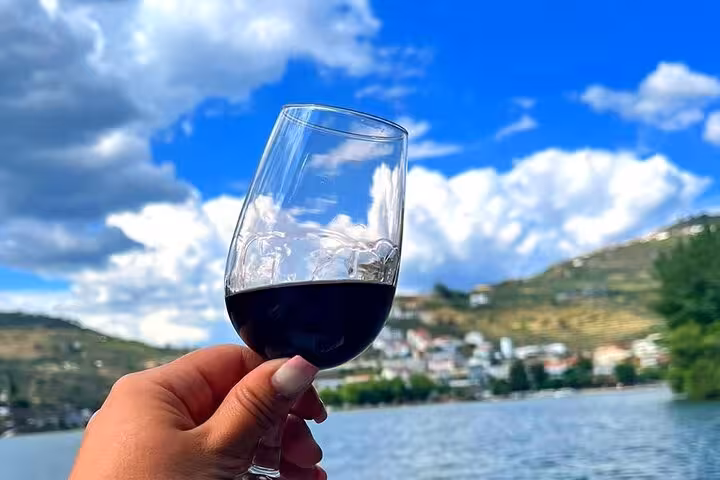 Hand holding a glass of Port wine on a 50-minute guided Douro River boat tour with vineyard views