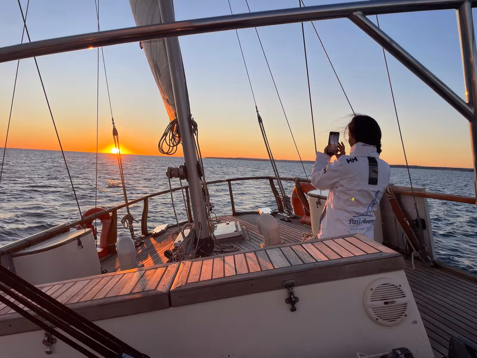 Guest photographing a stunning golden sunset from the deck of a romantic sailing tour in Portimao with sparkling wine
