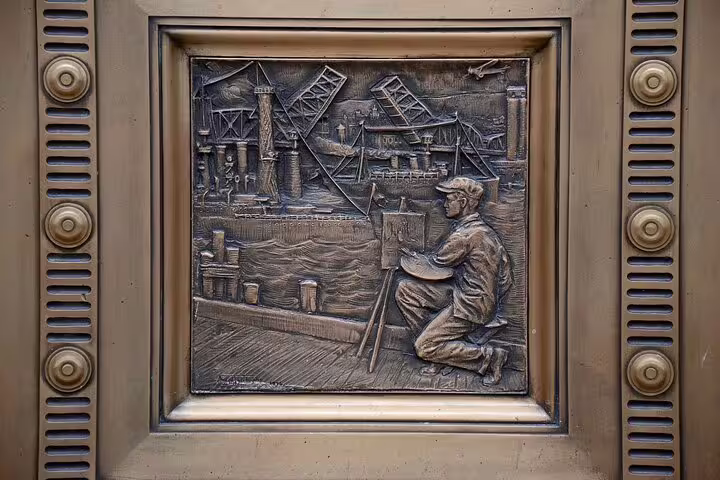 Bronze relief sculpture of artist painting harbor scene with industrial bridges and cranes in Portland
