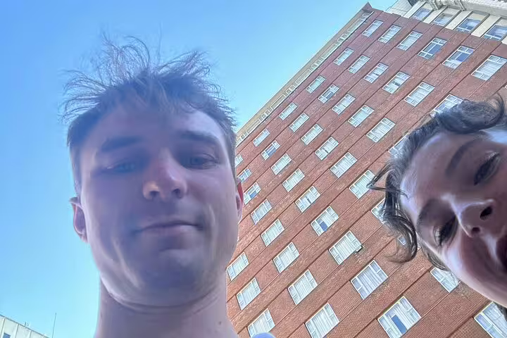 Two people taking a selfie in front of a tall red brick building on a sunny day in Portland