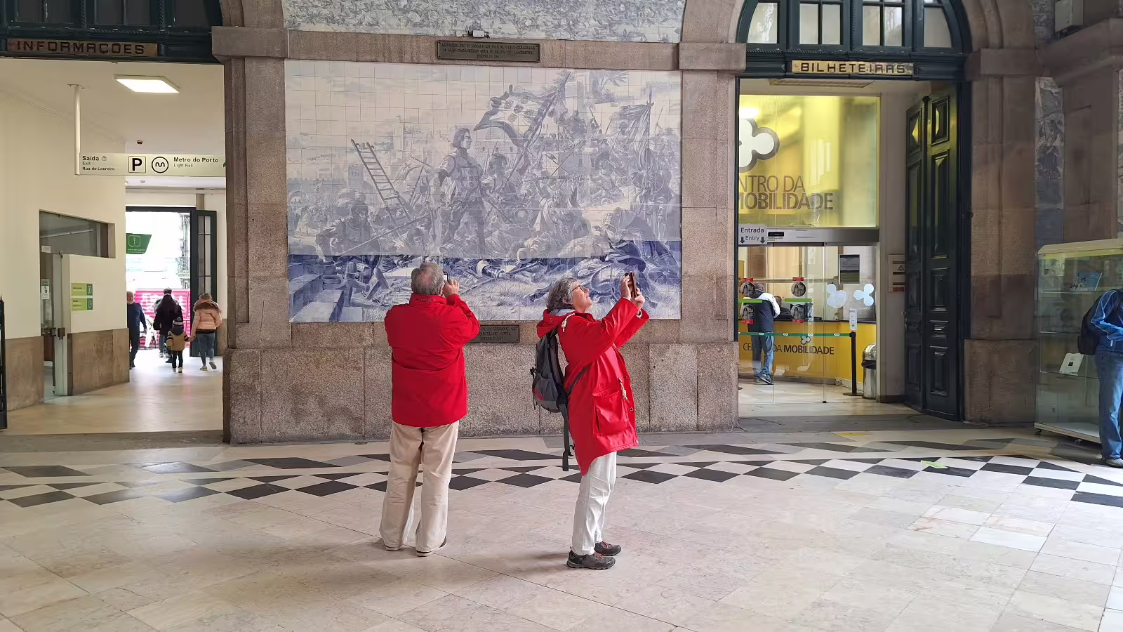 Visitors in red jackets admire azulejo tiles at São Bento Station, a highlight of Porto's private afternoon tour experience.
