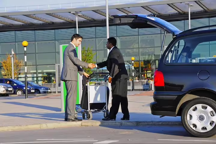 Professional driver assisting traveler with luggage at Porto Airport for private departure transfer service.