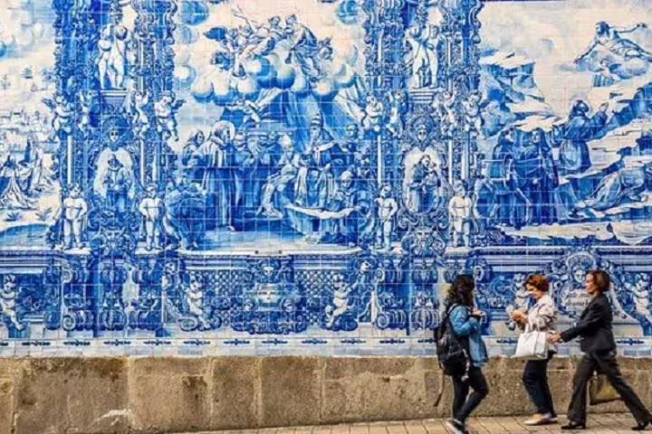 Visitors admire the intricate blue azulejos tiles adorning a historic wall in Porto, a highlight of the half-day tour.