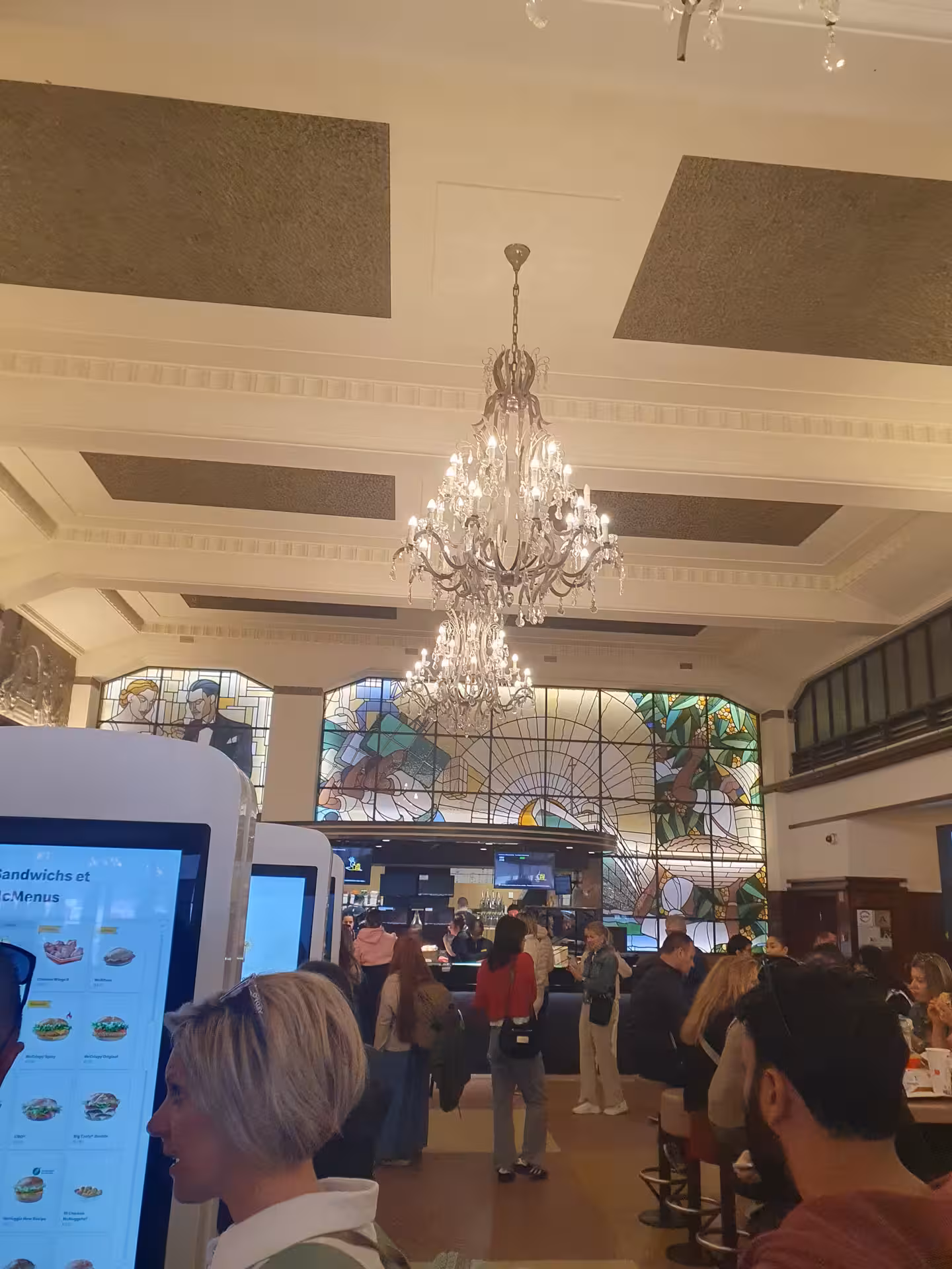 Interior of a bustling Porto café with elegant chandeliers and vibrant stained glass, offering a lively dining experience.