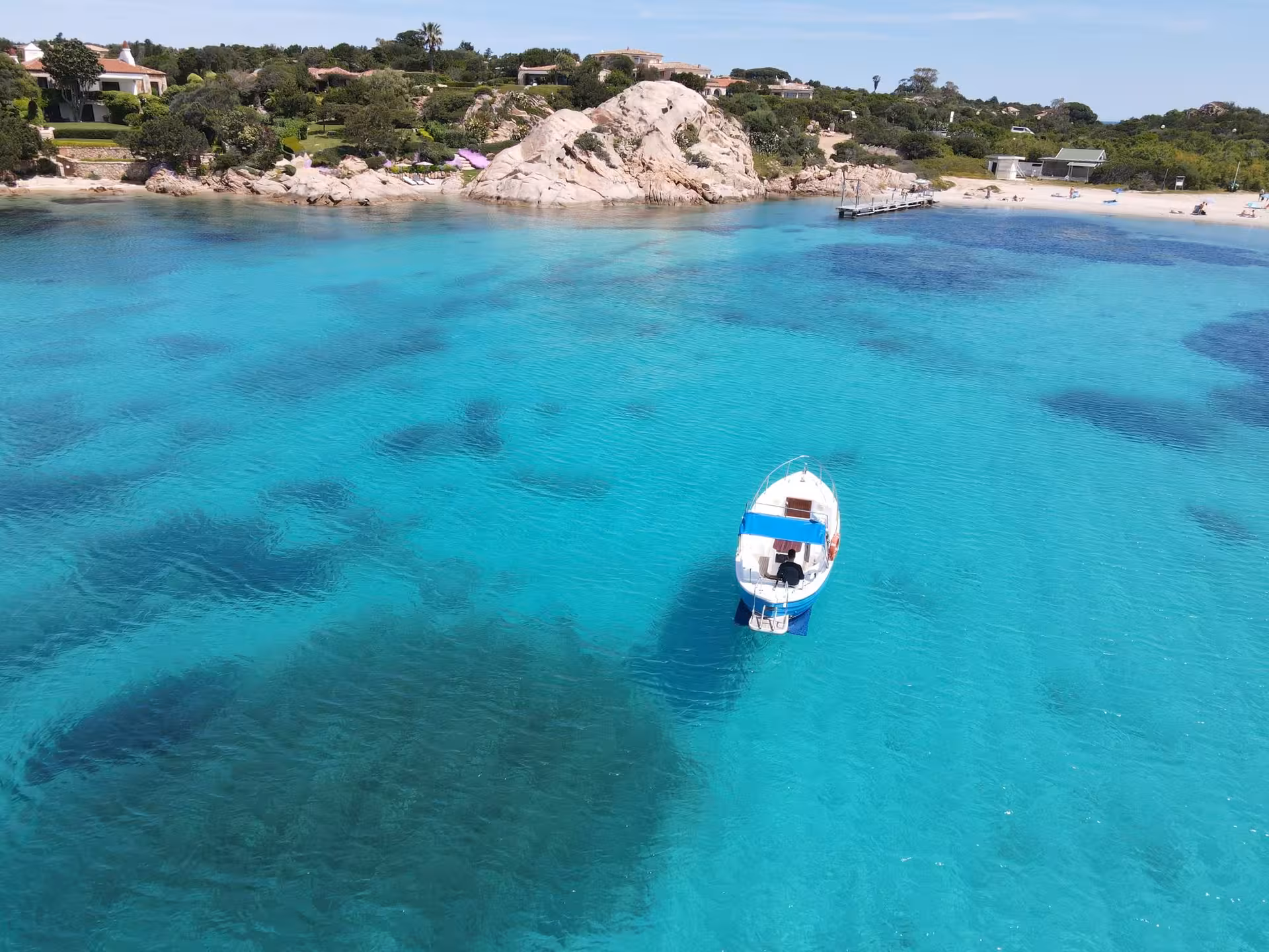 A boat anchored in crystal-clear waters near the rocky shores of Porto Cervo with lush greenery.