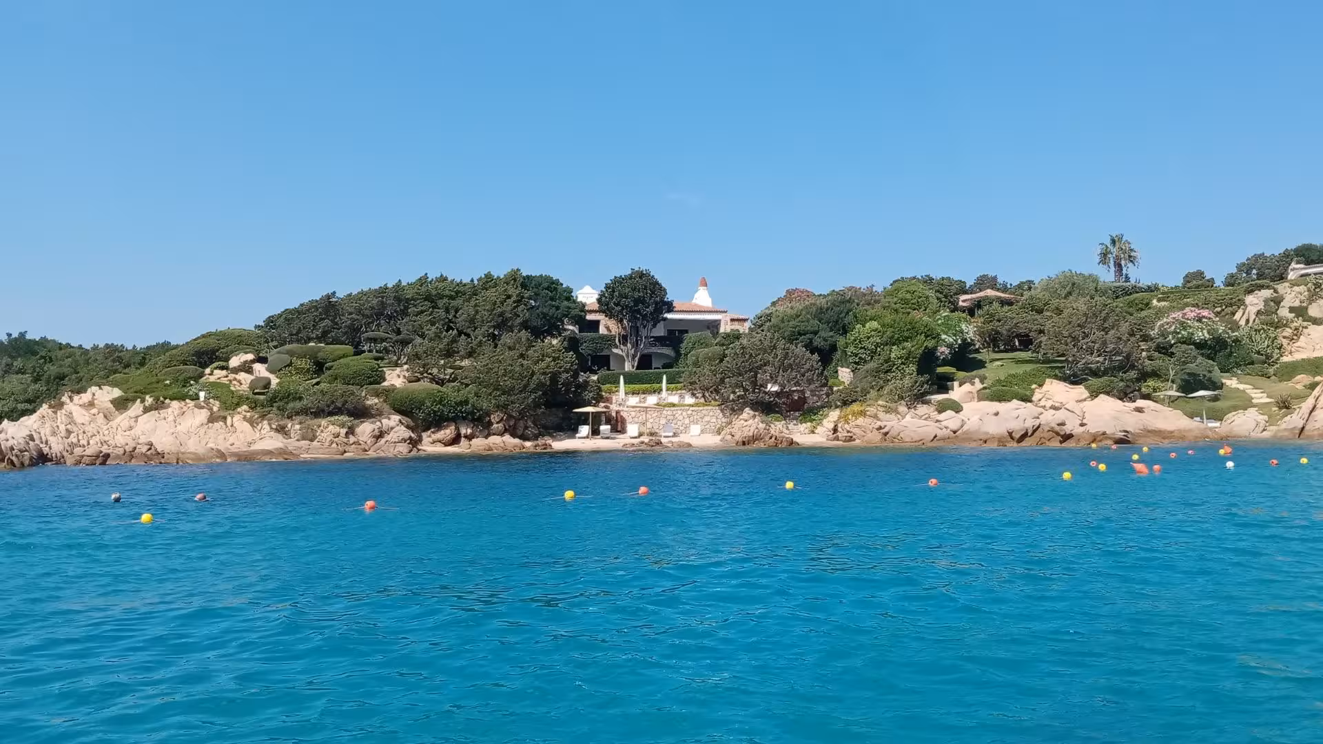 Scenic view of Porto Cervo's coastline with luxurious villas and clear blue waters on a sunny day.