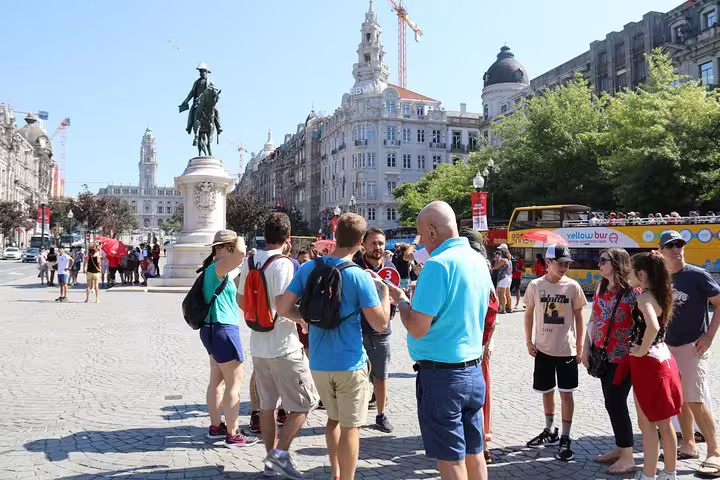 Tour group gathered around a statue in Porto's city square, highlighting landmarks on a guided half-day tour.