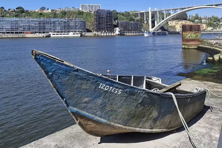 Vintage boat docked by the Douro River with a backdrop of Porto's modern architecture and iconic bridges.