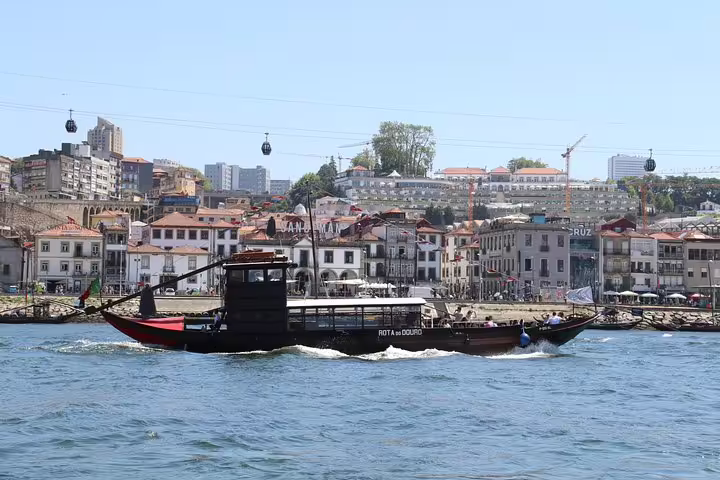Traditional boat cruising the Douro River with Porto's historic Ribeira district and cable cars in the background.