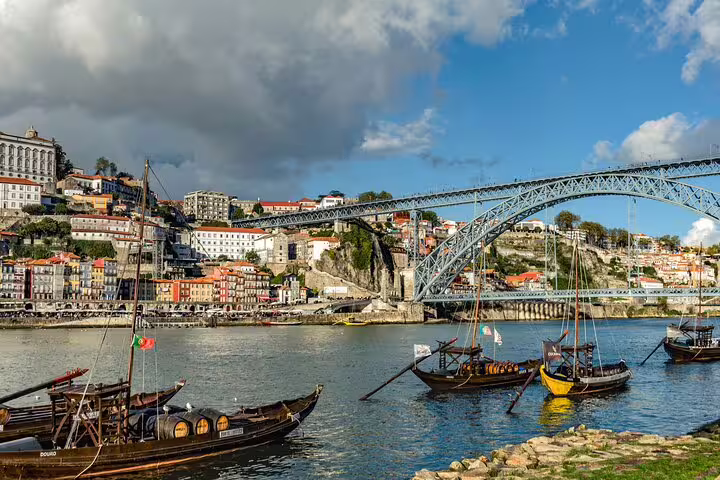 Traditional boats by the Douro River with the Dom Luís I Bridge in Porto, featured on a Lisbon private tour.