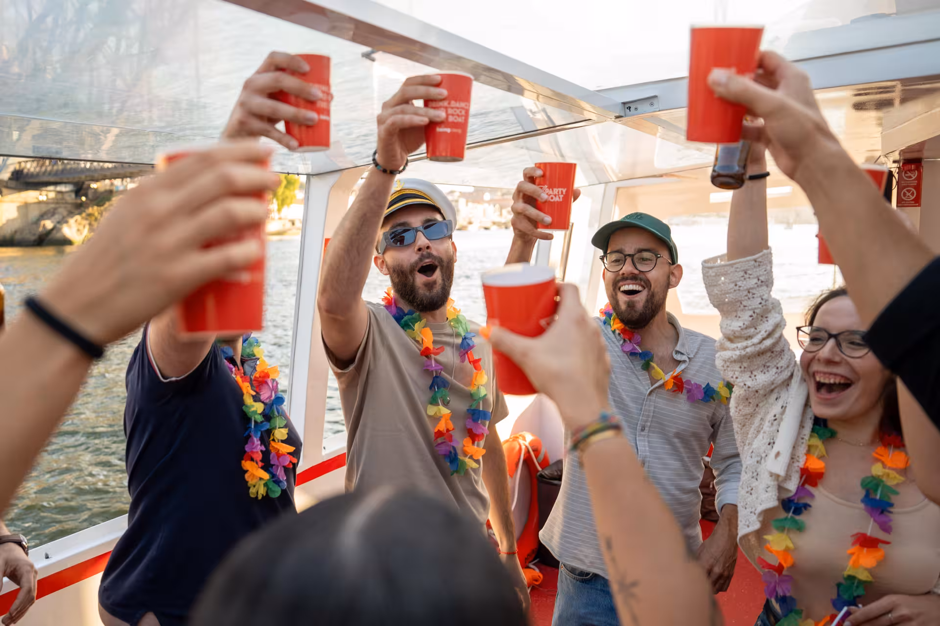 Group of friends toasting with drinks on a festive Douro River party boat in Porto, wearing colorful leis.