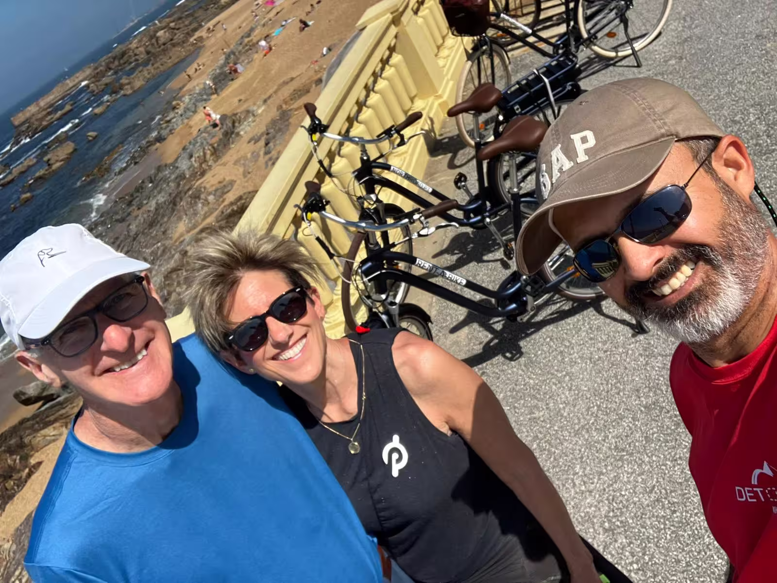 Group of friends smiling by the beach with e-bikes during Porto tour, capturing coastal adventure and sunny vibes.