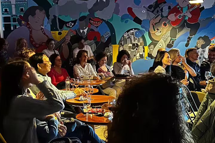 Audience enjoying live Fado music performance by the colorful riverfront in Porto, surrounded by lively mural art.