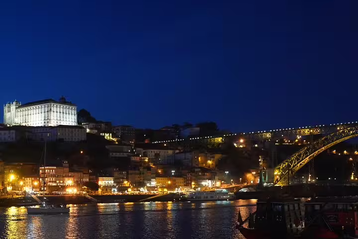 Scenic night view of Porto's illuminated riverside and iconic bridge, perfect for a private day trip from Lisbon tour.