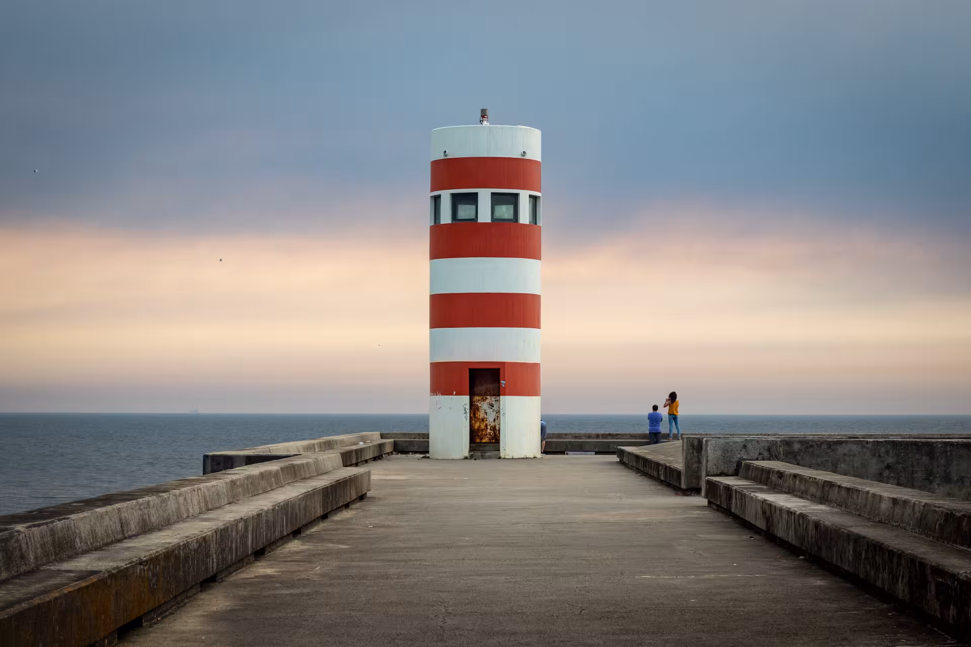 Tourists exploring Porto's iconic red and white striped lighthouse on a scenic coastal pier at sunset during a private e-bike tour.