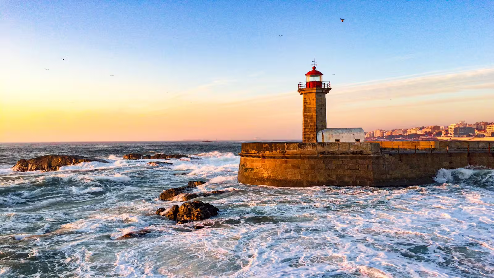 Sunset over Porto's iconic lighthouse, waves crashing against the rocks, perfect for a private night tour of Portugal's attractions.