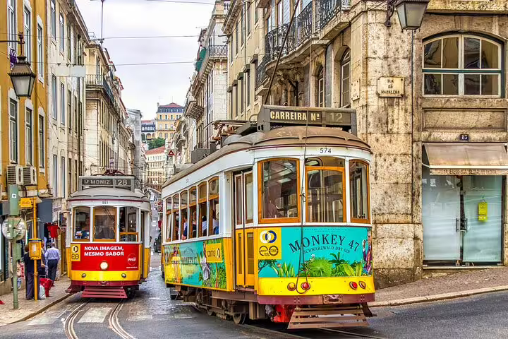 Iconic Lisbon trams navigate narrow streets, a highlight for travelers on a private transfer from Porto with city stops.