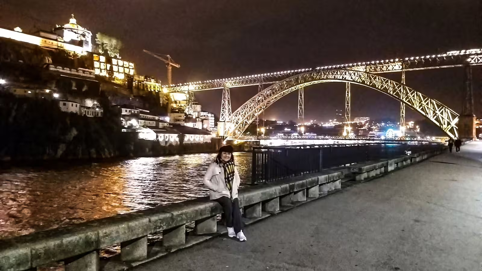 Woman enjoys a scenic night view of Porto's illuminated Dom Luís I Bridge and riverside on a private night tour.
