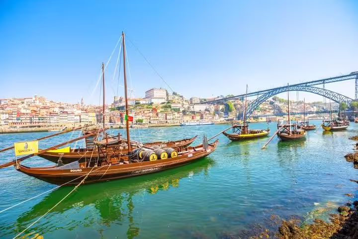 Traditional rabelo boats sailing on the Douro River with the iconic Porto bridge and cityscape in the background.