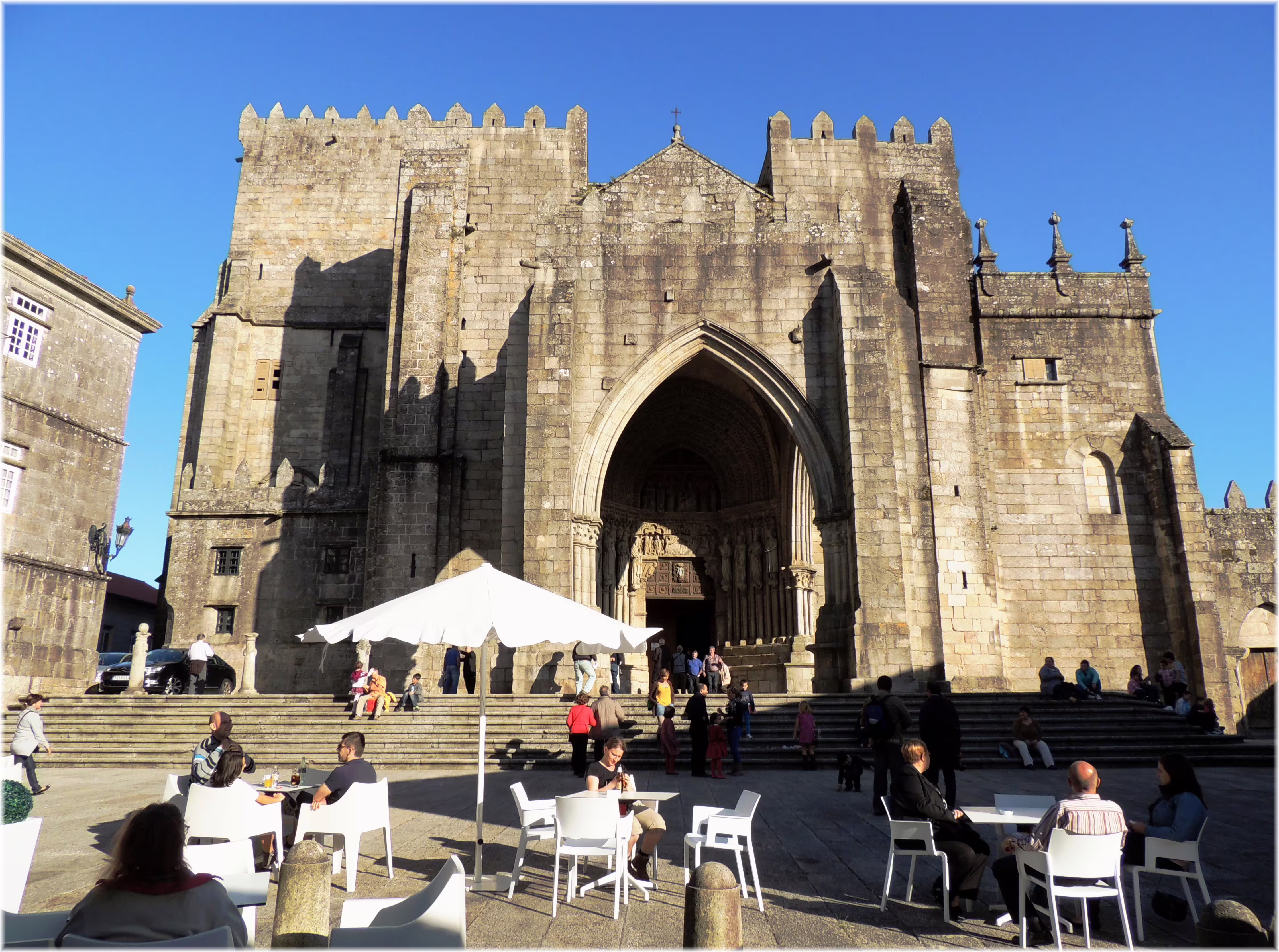 Historic cathedral facade in Pontevedra, Spain with outdoor café seating and visitors enjoying a sunny day.