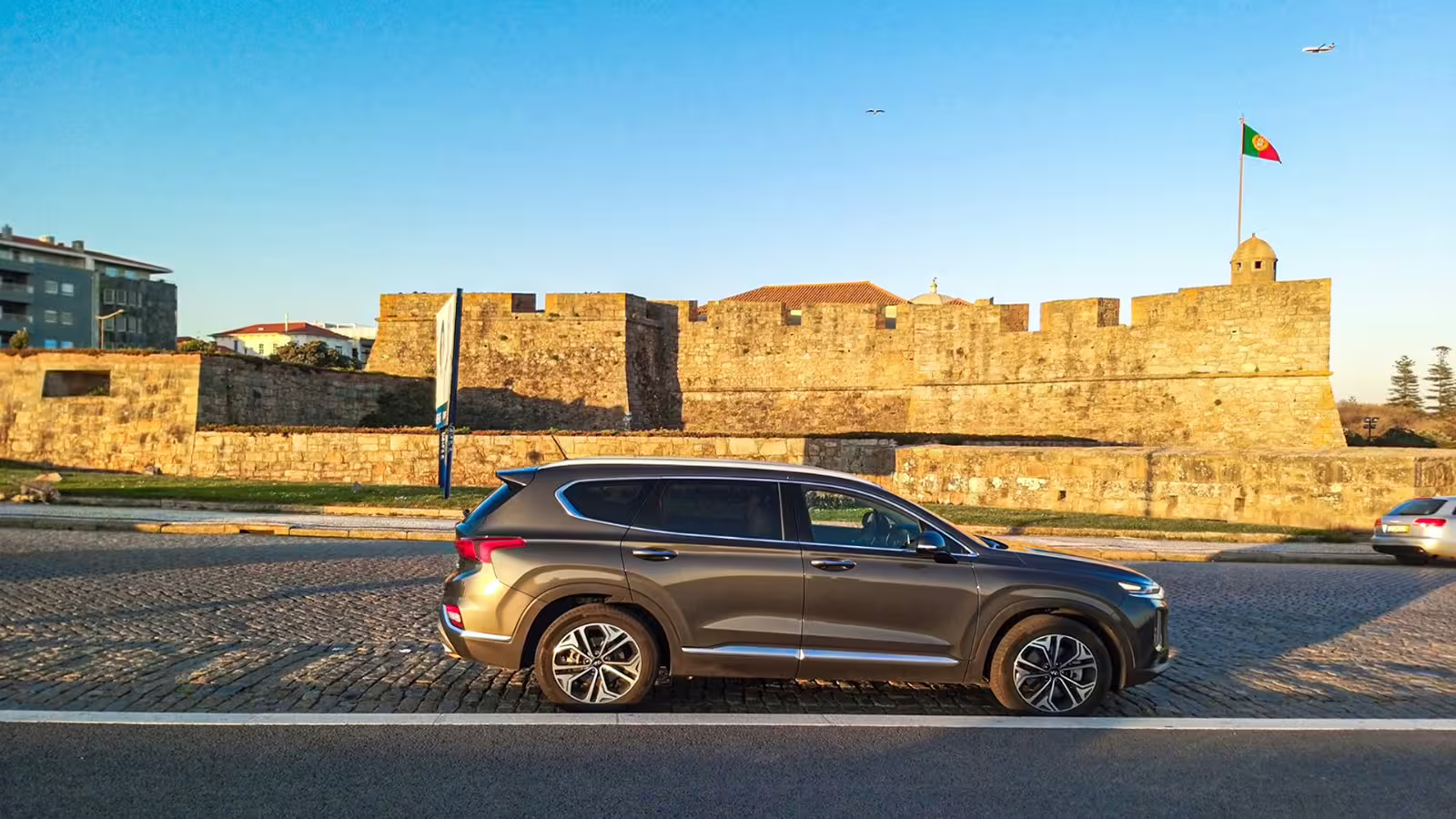 Modern SUV parked in front of historic Castelo do Queijo, Porto, showcasing iconic sights on a private night tour.