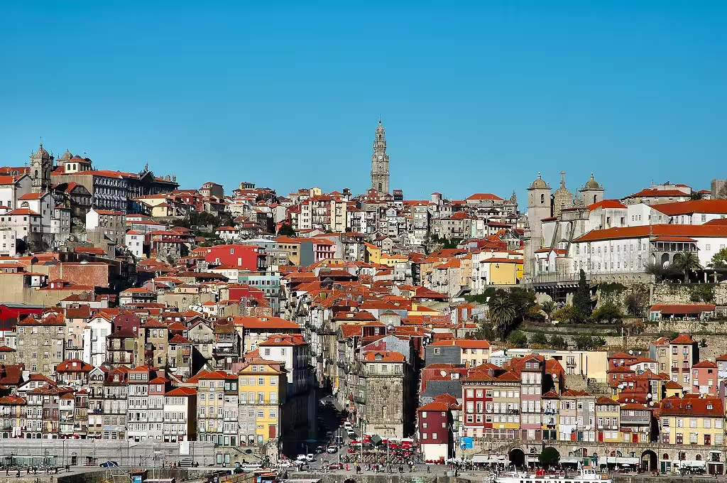 Panoramic view of Porto's vibrant Ribeira district, showcasing colorful historic buildings and the iconic Clerigos Tower under a clear blue sky.