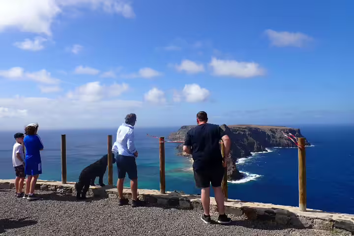 Tourists enjoying a panoramic view of Porto Santo's stunning coastline and cliffs during a half-day island tour under a clear blue sky.