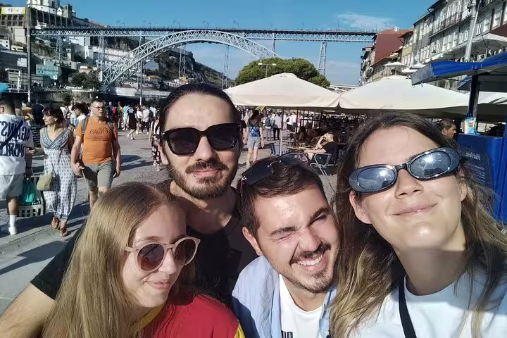 Group selfie at Ribeira waterfront with Dom Luís I Bridge during a Porto self-guided scavenger hunt tour