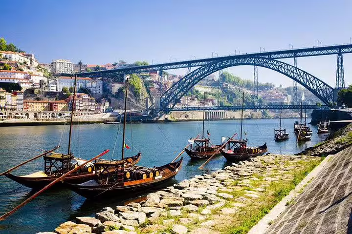 Traditional rabelo boats anchored by the Dom Luís I Bridge, a picturesque view on Porto's Six Bridges Cruise.