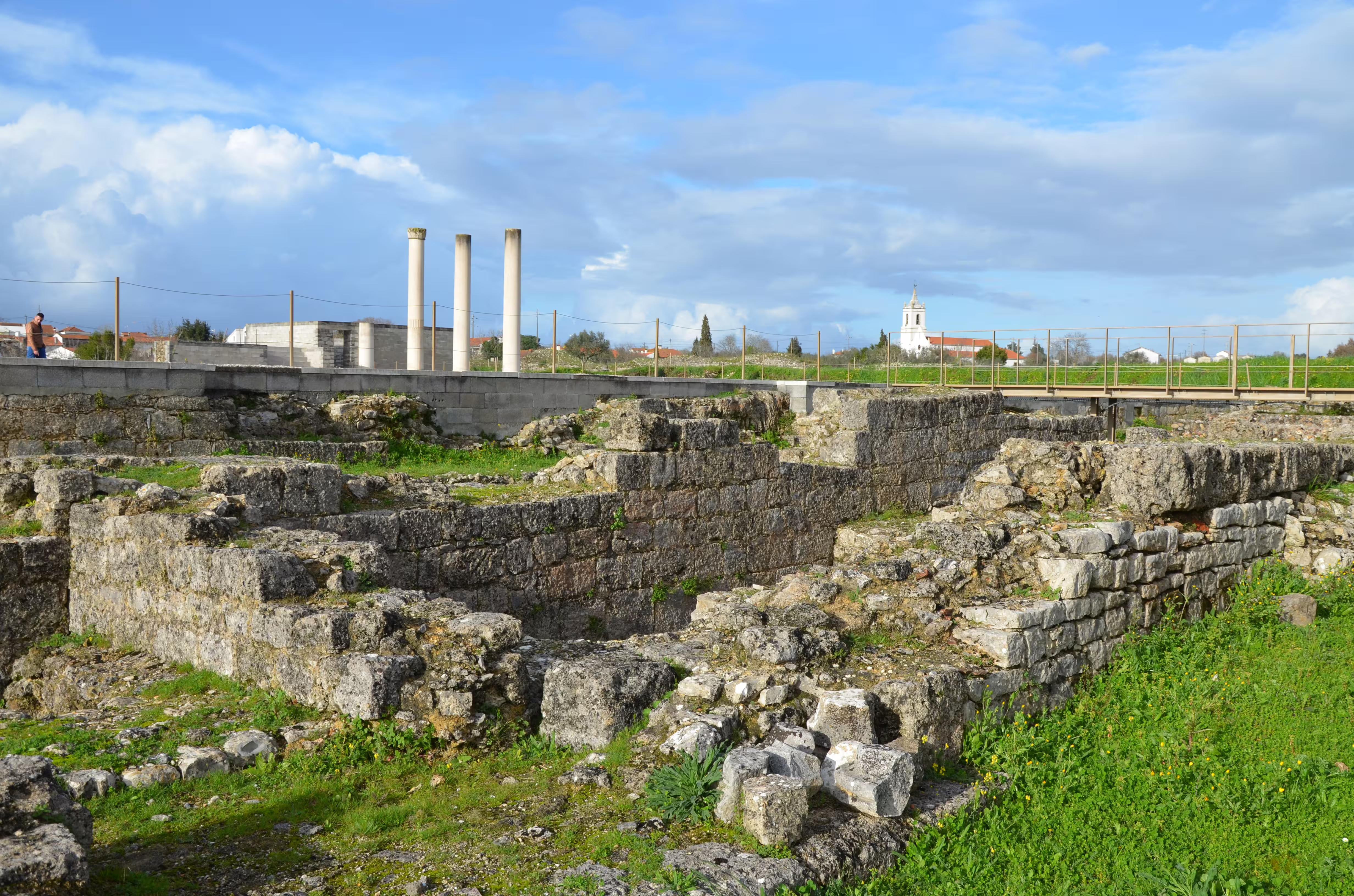 Ancient Roman ruins of Conímbriga with stone walls and columns under a partly cloudy sky.