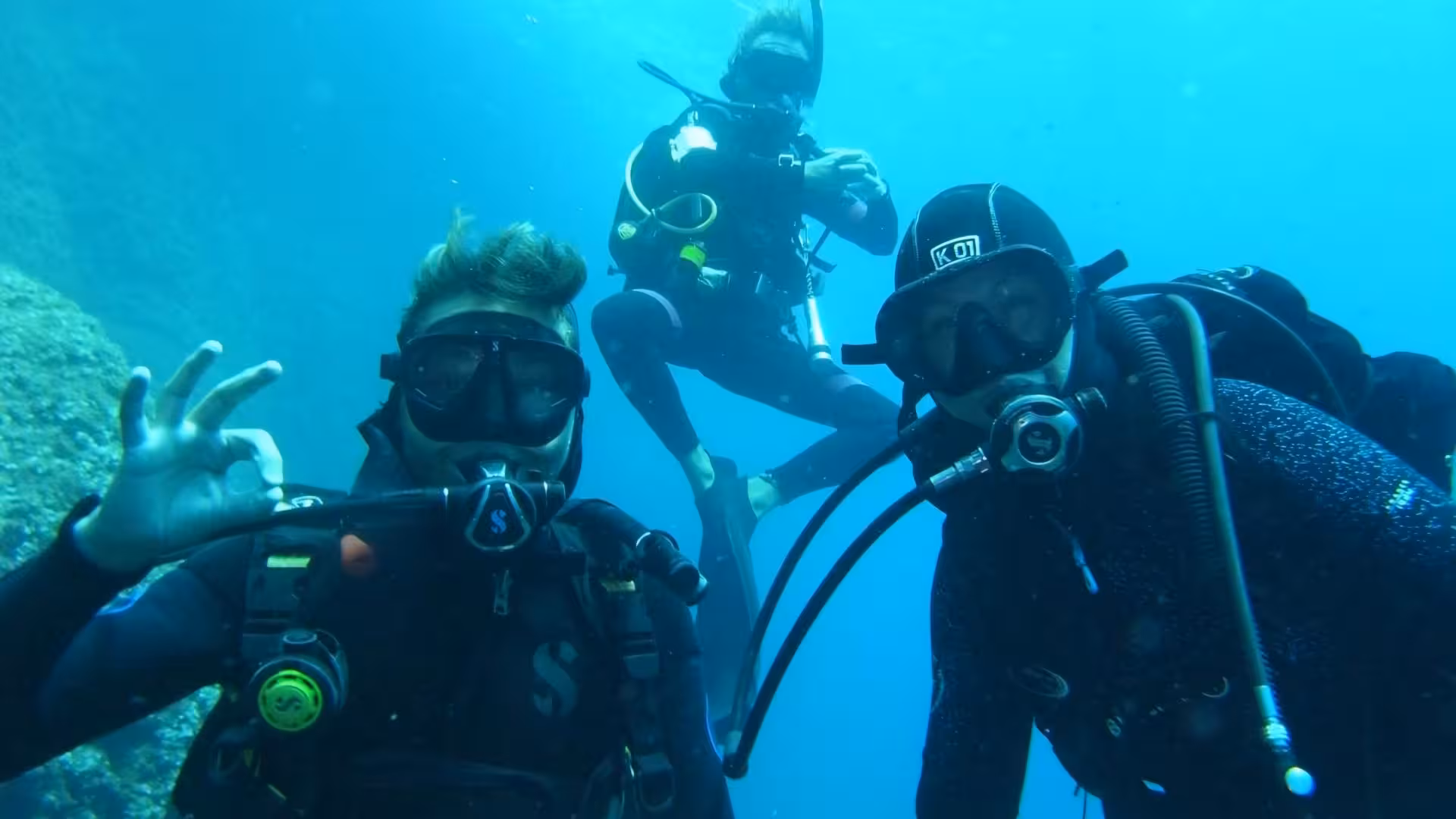 Three divers explore underwater depths in Porto Torres, showcasing diving baptism adventure for beginners.