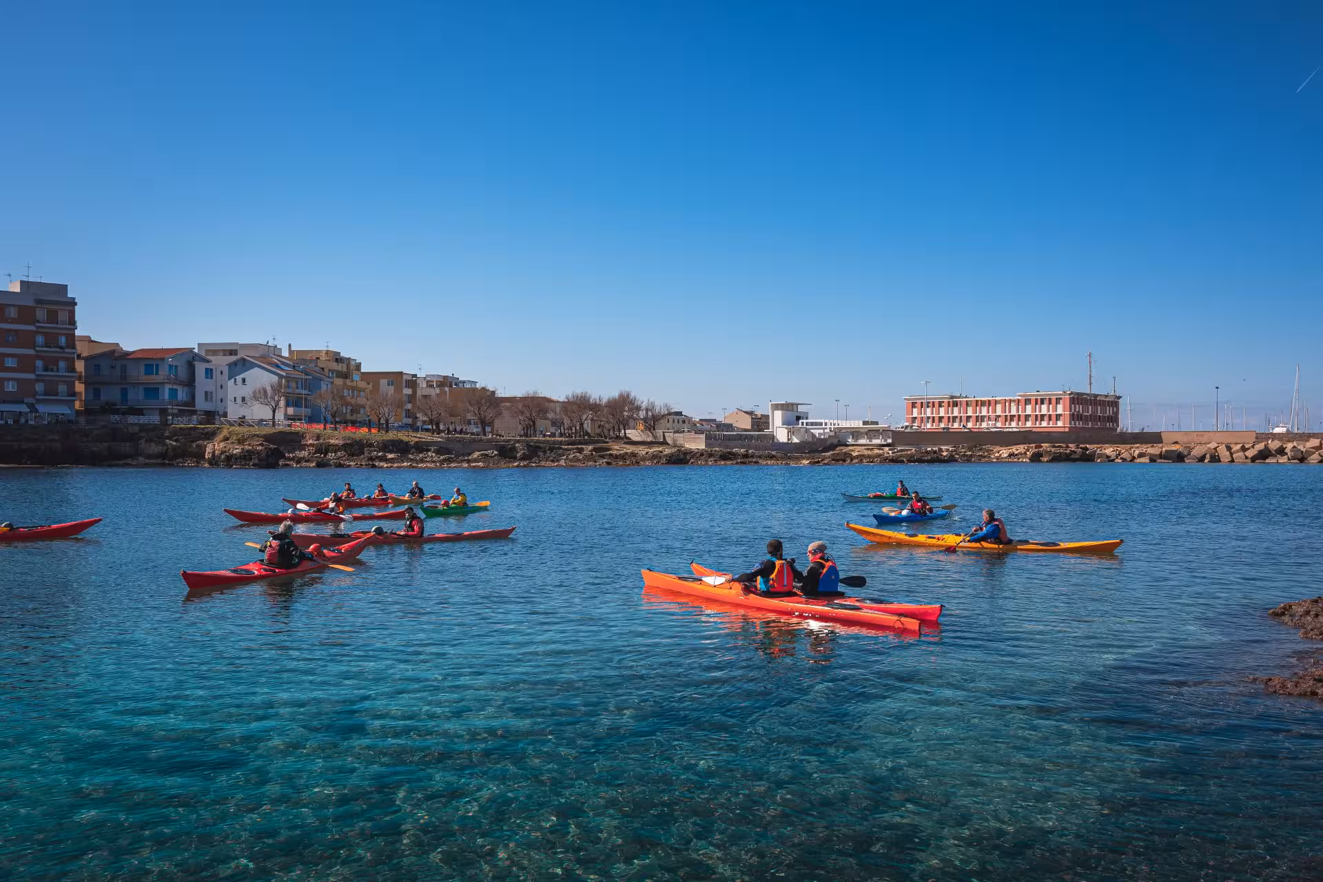 Group kayaking adventure in Porto Torres, navigating clear waters with scenic coastal views and vibrant kayaks.