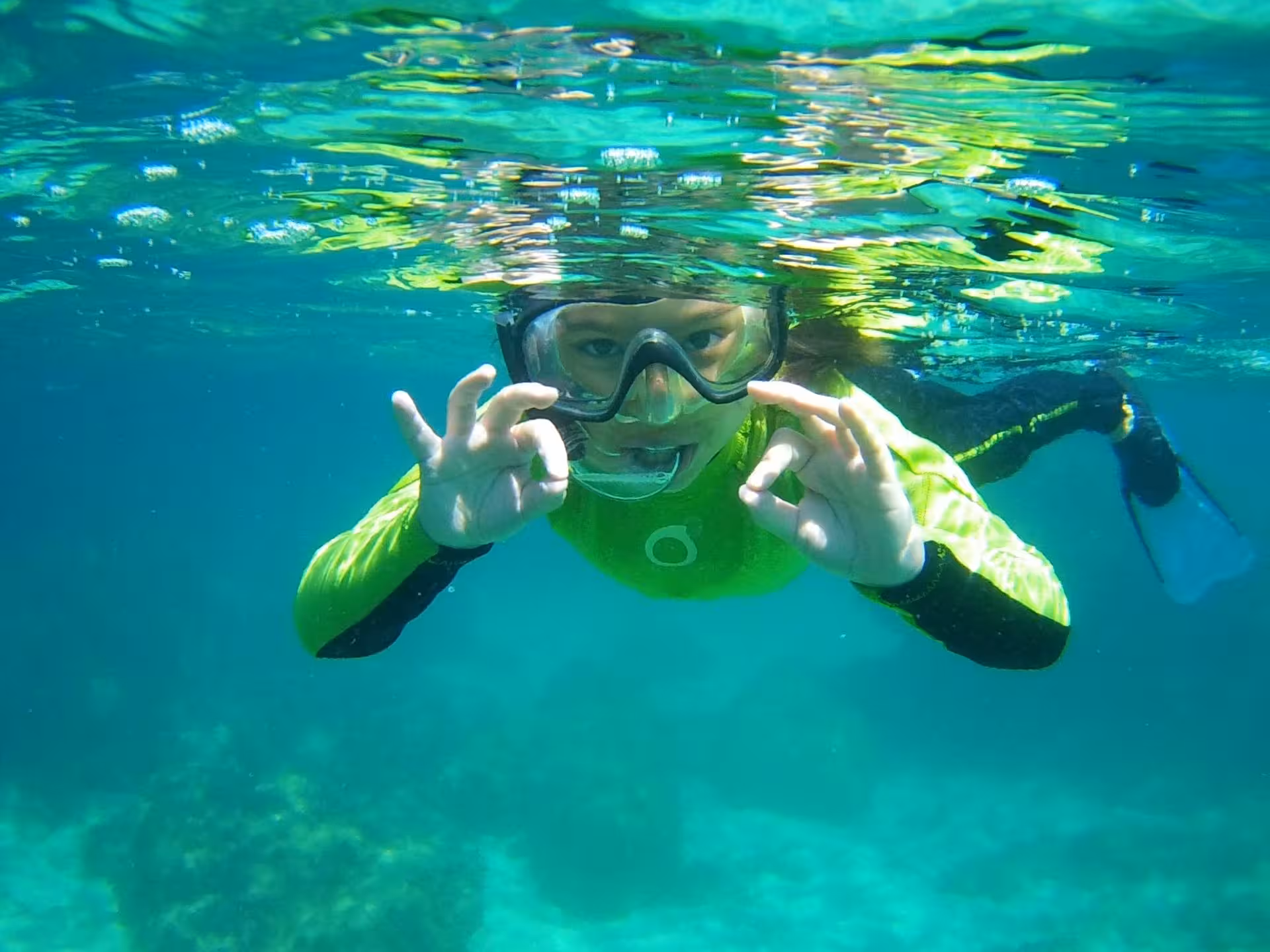 Snorkeler in neon gear gives an okay sign while exploring the crystal-clear waters of Porto Torres' Bay of Balai.