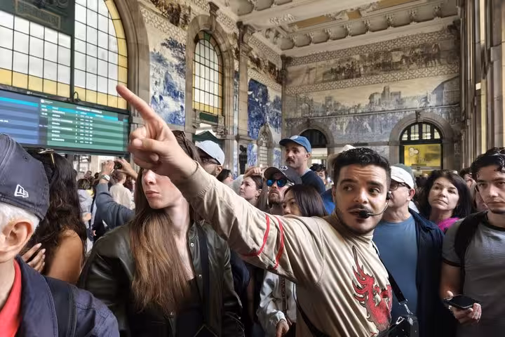 A lively tour guide with microphone points out historic azulejo tile panels to visitors inside Porto's grand São Bento Station.