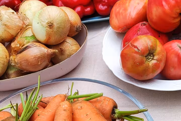 Assortment of fresh vegetables including onions, tomatoes, and carrots displayed on a table for a Portuguese cooking class.