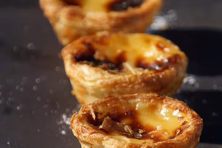 Close-up of traditional Portuguese custard tarts with golden, flaky crusts on a food and walking tour.