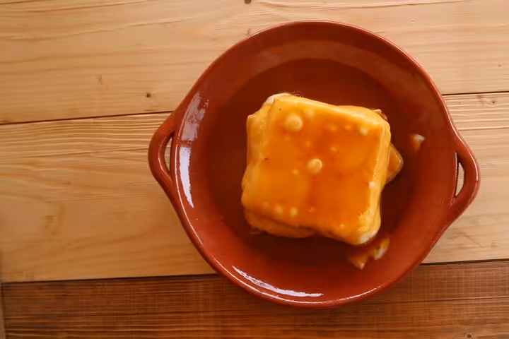 Traditional Portuguese francesinha in a rustic terracotta dish on a wooden table, capturing culinary delight on the terrace.