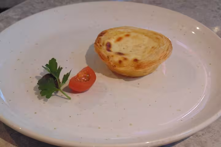 Traditional Portuguese pastry on a plate with a cherry tomato and parsley garnish, showcasing Sintra's delicacies.